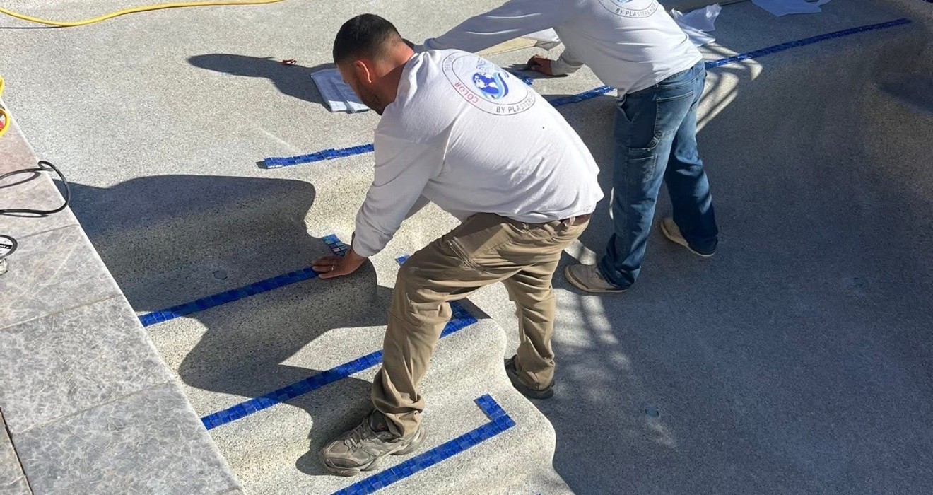 Workers installing blue mosaic tile on pool steps during a remodel